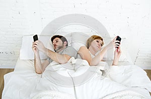 young married couple using their mobile phone in bed ignoring each other in relationship communication problems