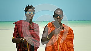 Young Masai Tribe Members in Red Dresses and Sunglasses Standing on Sand Beach of the Indian Ocean