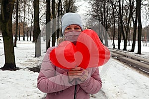 A young masked woman walks in a park with two red balls in the shape of hearts, close-up