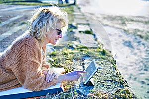 Young mature blonde woman relaxing outdoor with a tablet.