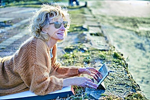 Young mature blonde woman relaxing outdoor with a tablet.