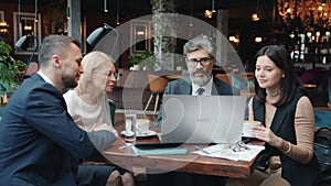 Young and mature businesspeople discussing project in restaurant using computer at table