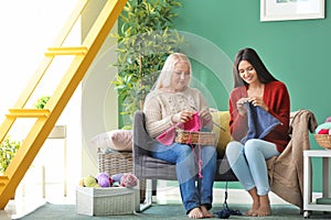 Young and mature women with knitting yarn sitting on sofa indoors