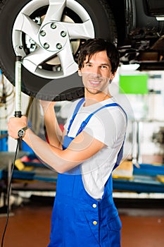 Young mechanic in blue overall working on car