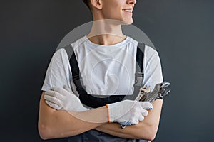 Young Mechanic with crossed arms and wrench standing on gray background