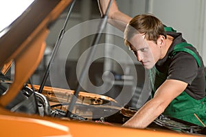 A young mechanic in a green overalls is repairing an auto engine