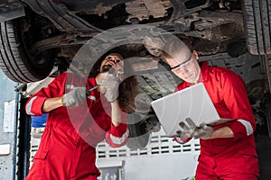 Young mechanics team in uniform are working in auto service with lifted vehicles. Car repair and maintenance concepts