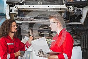 Young mechanics team in uniform are working in auto service with lifted vehicles. Car repair and maintenance concepts