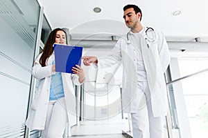 Young Medical Colleagues Analysing Paperboard While Walking Through Hospital