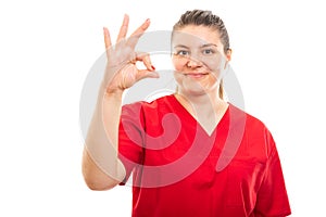 Young medical nurse wearing red scrub showing okay gesture