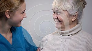 Young medical worker talking with smiling elderly lady in hospital, good news