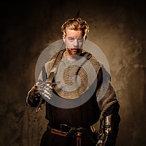 Young medieval knight posing on dark background.