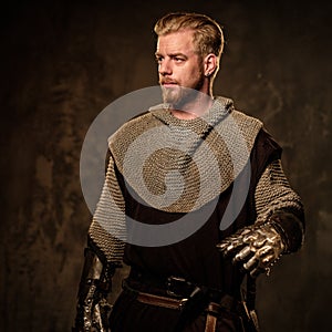 Young medieval knight posing on dark background.