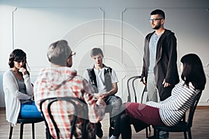 Young man admitting that he is an alcoholic during support group meeting photo