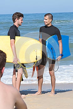 Young men carry bodyboards on shore