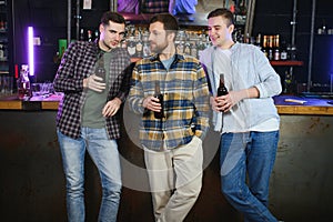 Young men in casual clothes are talking, laughing and drinking while sitting at bar counter in pub