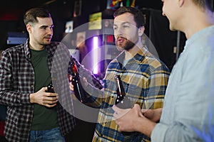 Young men in casual clothes are talking, laughing and drinking while sitting at bar counter in pub