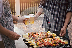 Young men cheers for a drink at a BBQ party between friends. Food, drink, people and family time concept