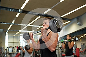 Young men flexing muscles with barbells in gym