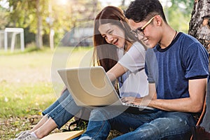 Young man and girls friend classmates sitting under tree consult