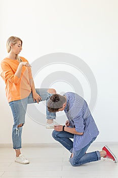 Young man is kneeling and reverently tying shoelaces to his domineering unidentified woman posing on a white background