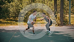 Young men playing basketball on the sports ground outdoors - a man dribbling avoiding his opponent