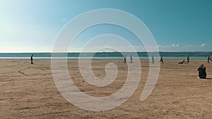 Young men playing soccer on a deserted beach near a river.