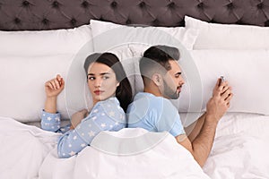 Young man preferring smartphone over his girlfriend in bed at home photo