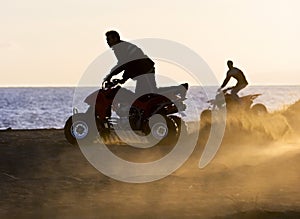 Young men on quad bikes on sandy beach during sunset