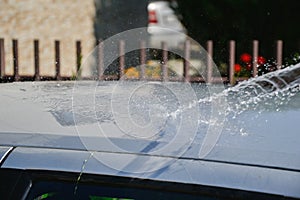 Young men washing silver car with pressured water and brush at sunny day. Close up of cleaning car on summer time
