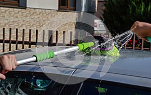 Young men washing silver car with pressured water and brush at sunny day. Close up of cleaning car on summer time