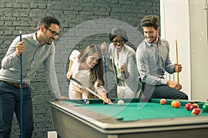 Young men and woman playing billiards at office after work.