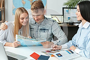 Young couple in a tour agency communication with a travel agent travelling concept holding booklet photo