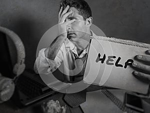 Young messy and depressed business man showing notepad asking for help desperate and sad at office laptop computer desk looking ov