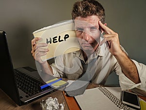 Young messy and depressed business man showing notepad asking for help desperate and sad at office laptop computer desk looking ov