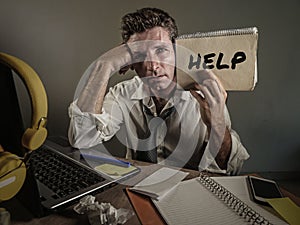 Young messy and depressed business man showing notepad asking for help desperate and sad at office laptop computer desk looking ov