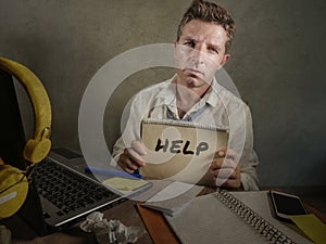 Young messy and depressed business man showing notepad asking for help desperate and sad at office laptop computer desk looking ov