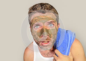 Young messy funny man looking at himself horrified in bathroom mirror with green cream on his face applying beauty facial mask pro