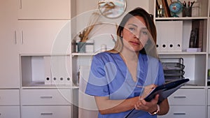 Young mexican female medic in uniform holding clipboard in doctor`s office