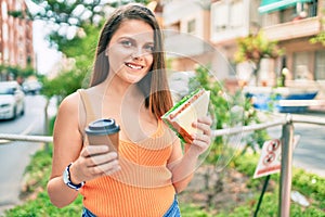 Young middle east girl eating sandwich and drinking take away coffee at the city