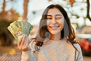 Young middle east girl smiling happy holding chile pesos banknotes at the city