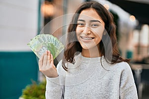 Young middle east girl smiling happy holding chile pesos banknotes at the city