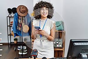 Young middle east shopkeeper woman smiling happy using smartphone at clothing store
