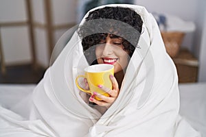 Young middle east woman drinking cup of coffee sitting on bed at bedroom