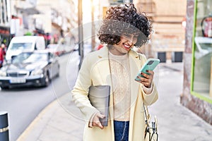 Young middle east woman excutive using smartphone holding laptop at street