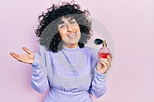 Young middle east woman holding perfume celebrating achievement with happy smile and winner expression with raised hand