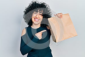 Young middle east woman holding take away paper bag smiling happy pointing with hand and finger