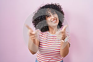 Young middle east woman standing over pink background pointing fingers to camera with happy and funny face