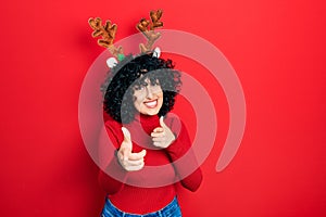 Young middle east woman wearing cute christmas reindeer horns pointing fingers to camera with happy and funny face photo