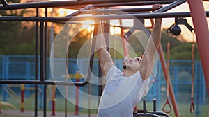 Young middle eastern guy doing pull-ups exercises during workout at city sports ground outdoors. Handsome strong